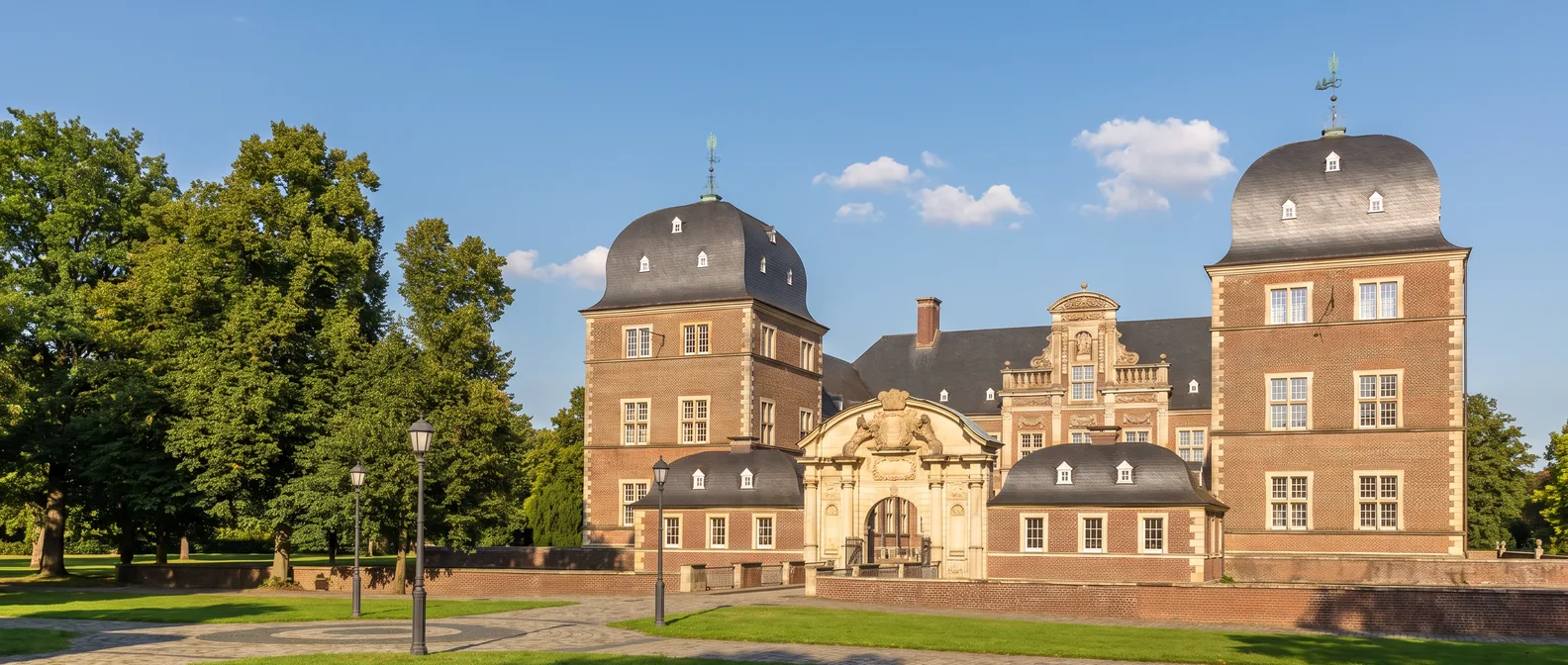 Das barocke Wasserschloss Ahaus aus rotem Backstein mit zwei Ecktürmen mit geschwungenen Schieferhauben und Sandsteinportal im Abendlicht