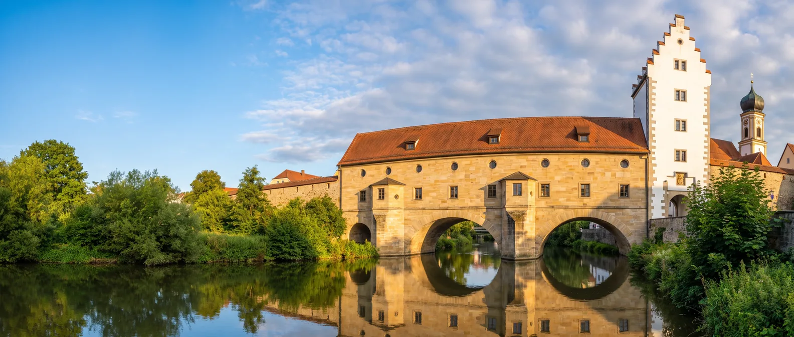 Die Stadtbrille in Amberg: Stadtmauerbau mit zwei Bögen über der Vils, die sich im Wasser zu zwei Kreisen spiegeln