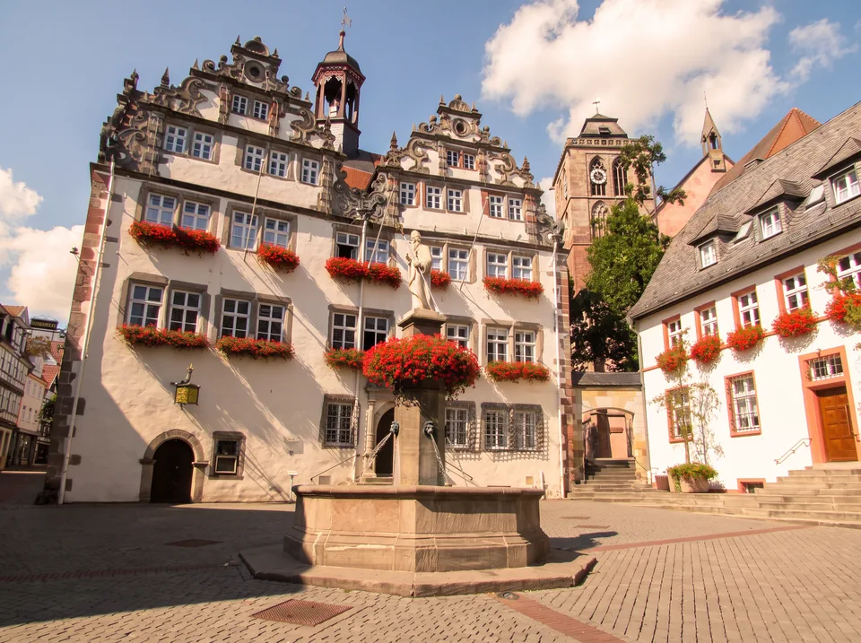 Das weiße Rathaus von Bad Hersfeld mit verzierten Renaissance-Giebeln, rotem Blumenschmuck und Brunnen davor
