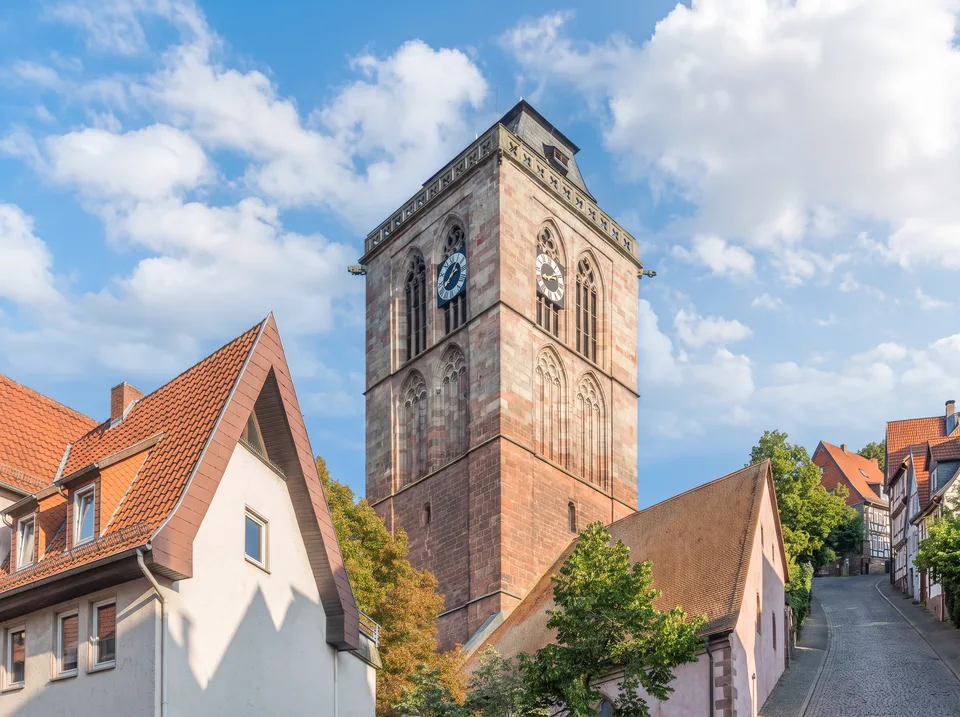 Der hohe gotische Sandsteinturm der Stadtkirche in Bad Hersfeld mit Uhr und Spitzbogenfenstern über den Dächern der Altstadt