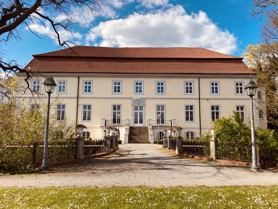 Hell verputztes Schloss Ovelgönne mit rotem Walmdach, Freitreppe, Laternen und Kiesauffahrt im Frühlingslicht