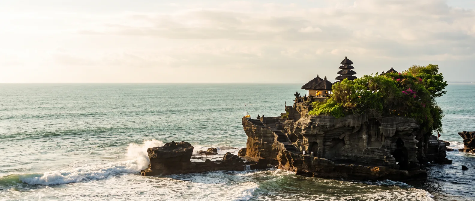 Der Meerestempel Pura Tanah Lot mit strohgedeckten Schreinen auf einem bewachsenen Felsen in der Brandung vor der Südwestküste Balis
