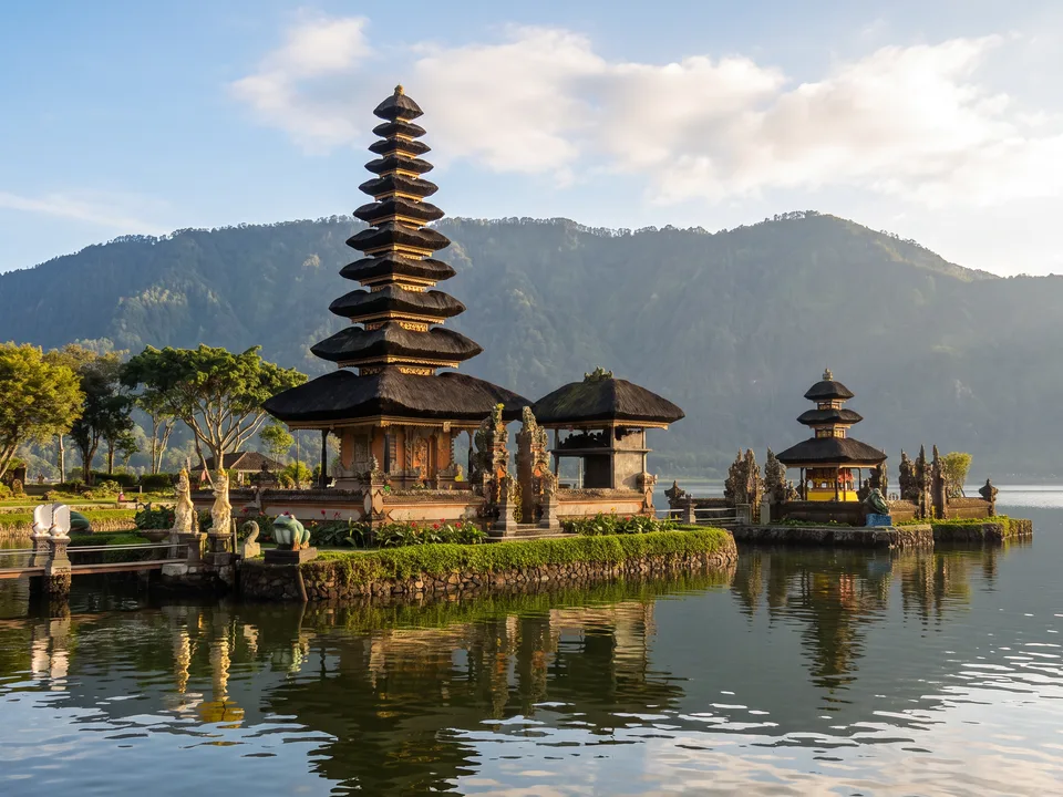 Der Tempel Pura Ulun Danu Bratan mit mehrstufiger Meru-Pagode auf einer kleinen Insel im Bratansee, dahinter bewaldete Berge