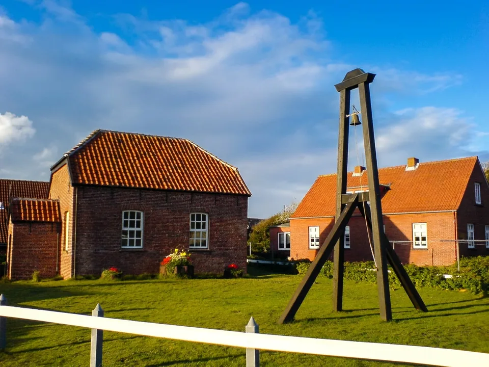 Alte Inselkirche auf Baltrum aus rotem Backstein mit dem hölzernen Glockengerüst der Inselglocke auf der Wiese davor