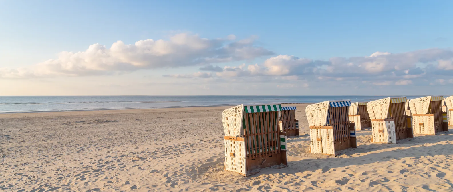 Weiße Strandkörbe mit gestreiften Markisen am breiten Sandstrand von Baltrum, dahinter die Nordsee im goldenen Nachmittagslicht