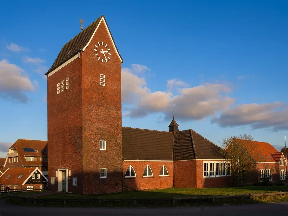 Große evangelisch-lutherische Inselkirche auf Baltrum mit hohem Backsteinturm, Turmuhr und Kirchenschiff unter blauem Himmel