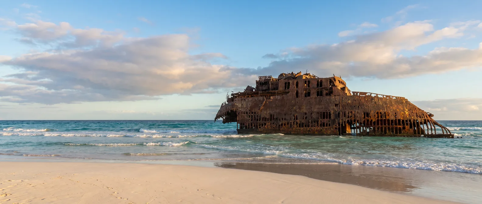 Das rostige Wrack der Cabo Santa Maria in der türkisfarbenen Brandung vor dem hellen Sandstrand von Boa Vista im Abendlicht