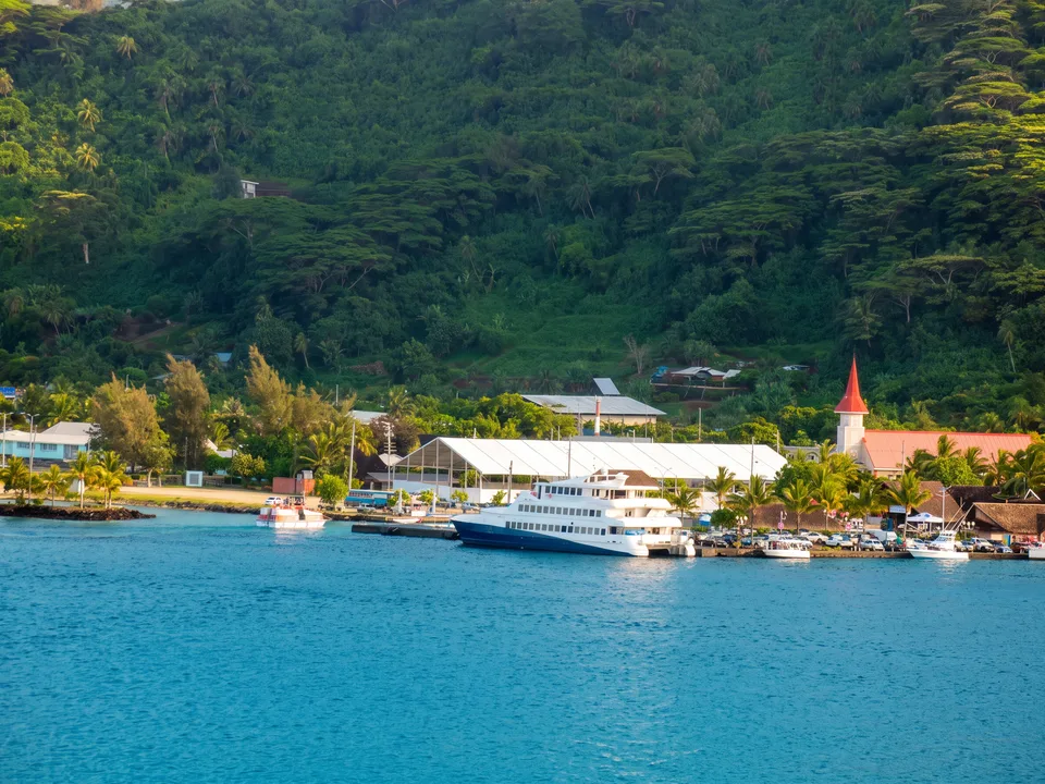 Hafen von Vaitape auf Bora Bora mit Fähre, weißen Hallen, Kirchturm und bewaldetem Berghang