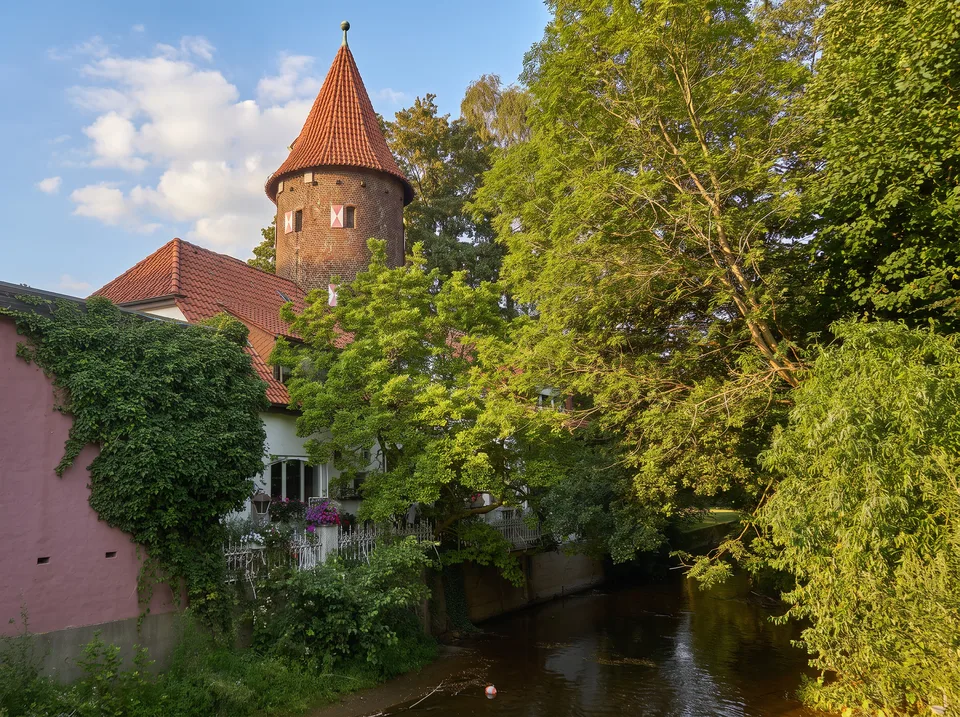 Der runde Kuhmturm aus Backstein mit rotem Kegeldach in Borken über grünen Bäumen an der Aa