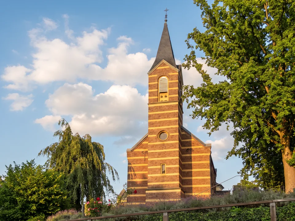 Die Alte evangelische Kirche in Bornheim mit gestreifter Backsteinfassade und spitzem Turm zwischen Bäumen