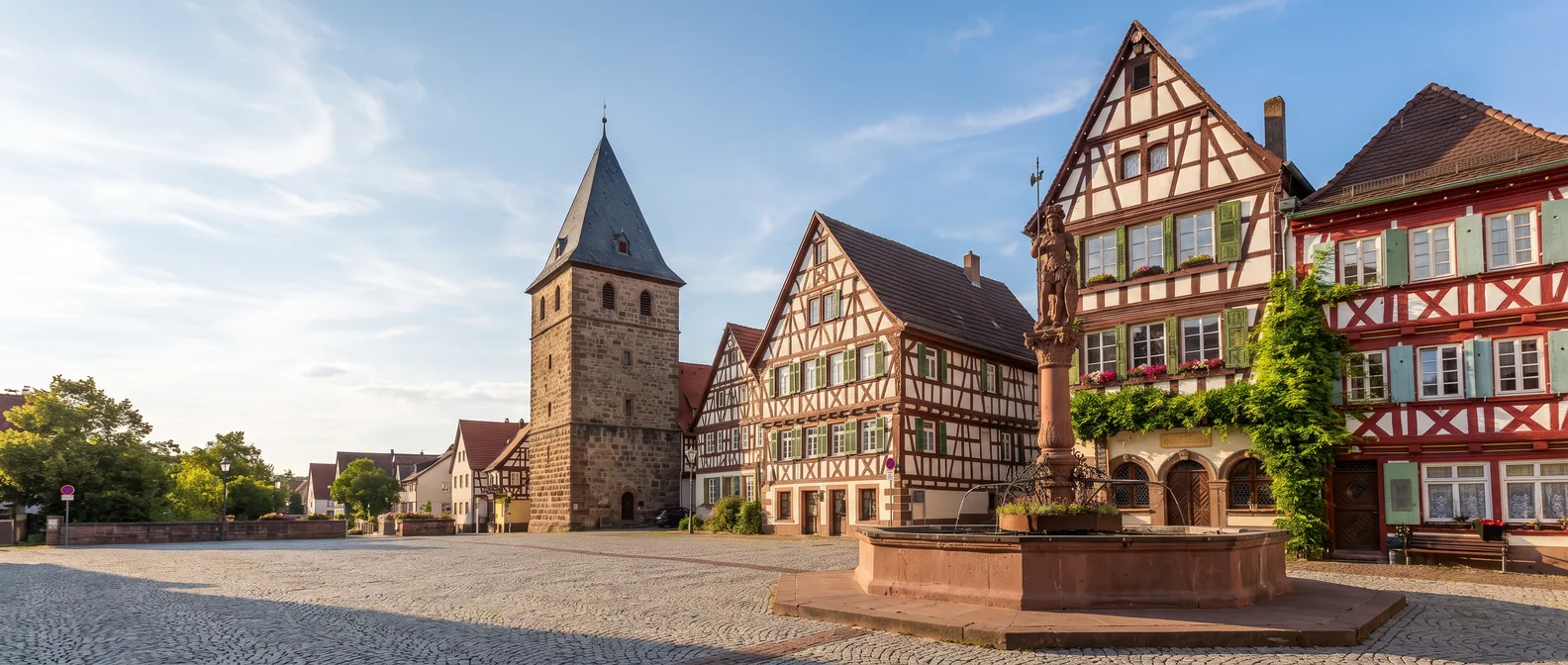 Marktplatz in Bretten mit rotem Sandstein-Marktbrunnen, Fachwerkhäusern und dem Pfeiferturm im Hintergrund unter blauem Himmel