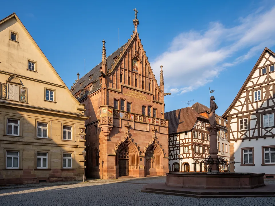Das Melanchthonhaus in Bretten mit neugotischer roter Sandsteinfassade und Ziergiebel am Marktplatz, daneben Fachwerkhäuser und der Marktbrunnen