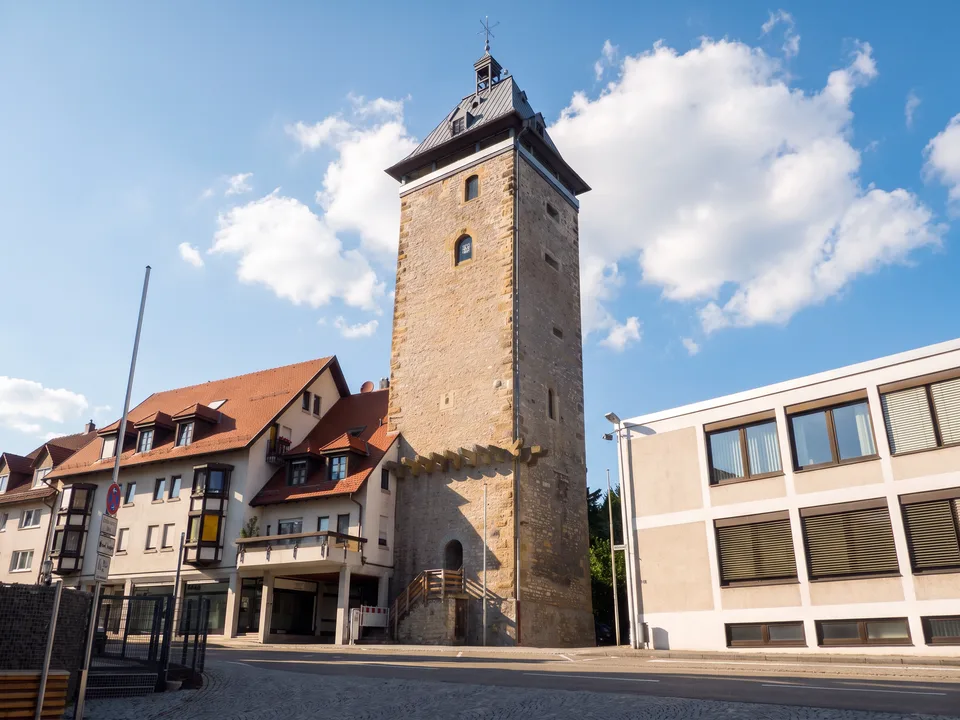 Der Pfeiferturm in Bretten, ein hoher Sandsteinturm mit Schieferhaube, im Sonnenlicht vor blauem Himmel