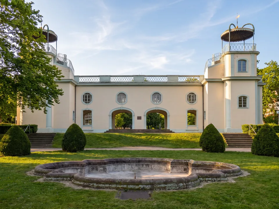 Das helle Belvedere im Bruchsaler Stadtgarten mit zwei Ecktürmen und runden Aussichtsplattformen, davor ein Brunnenbecken