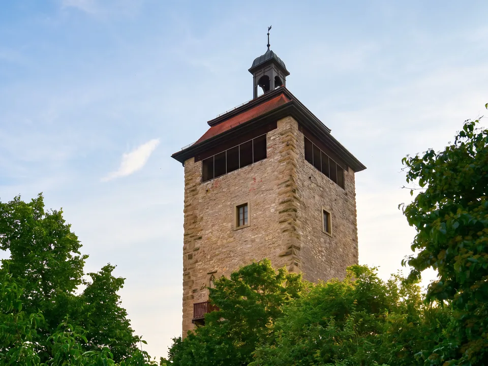 Der mittelalterliche Bergfried in Bruchsal aus Sandstein mit rotem Dach und kleinem Glockentürmchen zwischen Bäumen