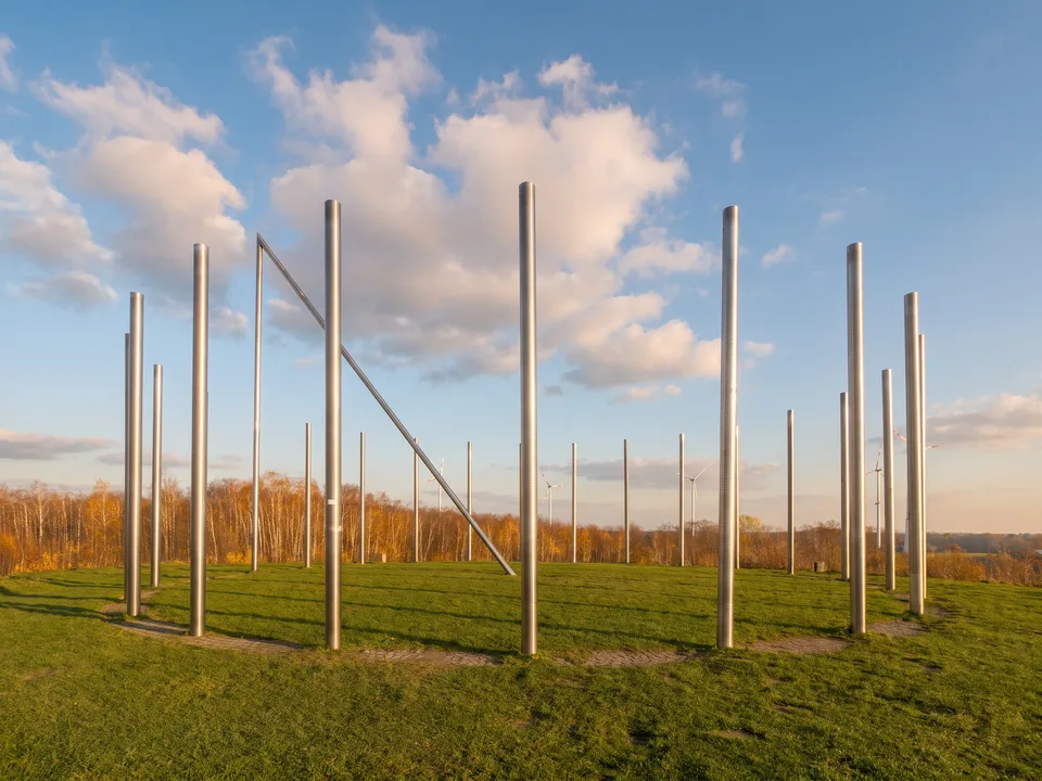 Kreis aus hohen Edelstahlstelen der Sonnenuhr auf dem Gipfel der Halde Schwerin unter blauem Himmel mit Wolken