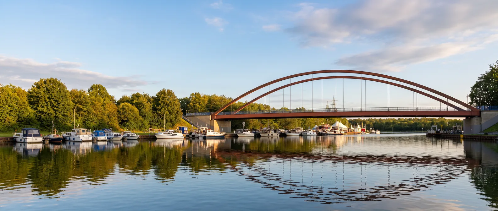 Die rote Stahlbogenbrücke über dem Dortmund-Ems-Kanal am Dattelner Hafen mit Booten und Spiegelungen im Abendlicht