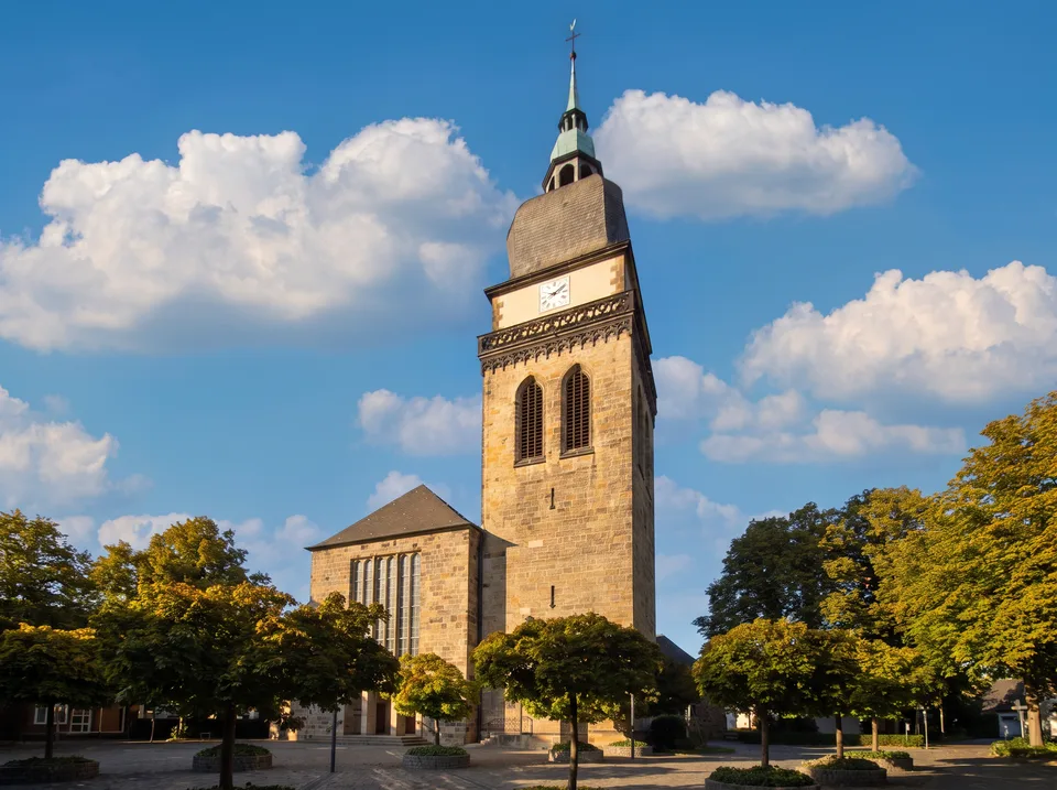 Die Pfarrkirche St. Amandus in Datteln mit hohem Sandsteinturm, Schieferhaube und grüner Laterne zwischen Bäumen