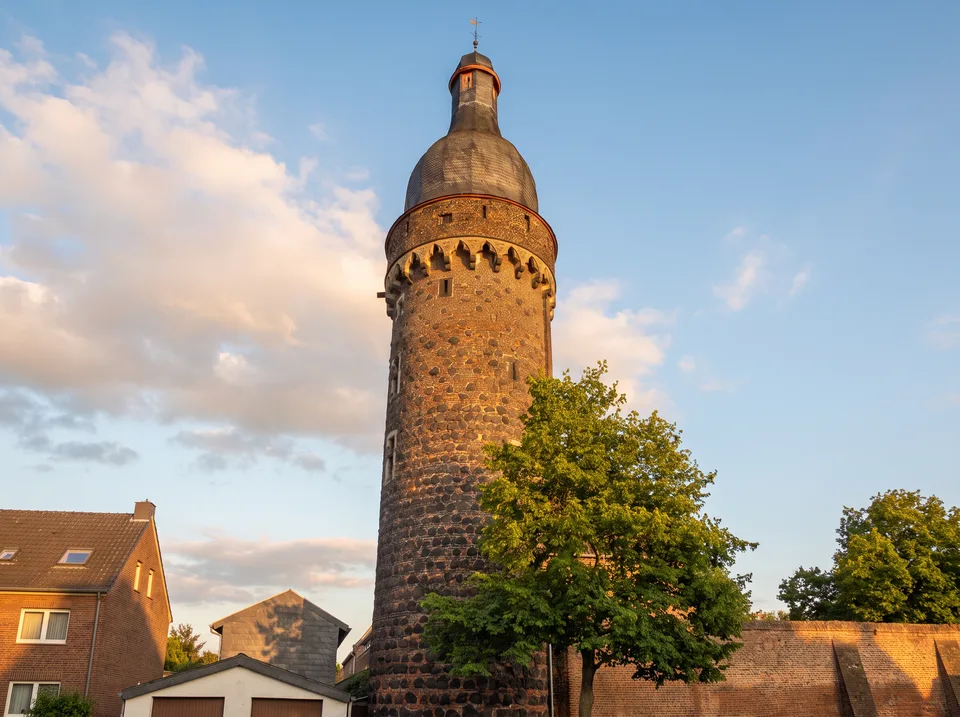 Der runde Juddeturm in Zons aus Basalt und Backstein mit Zinnenkranz und barocker Haube neben der Stadtmauer unter blauem Himmel