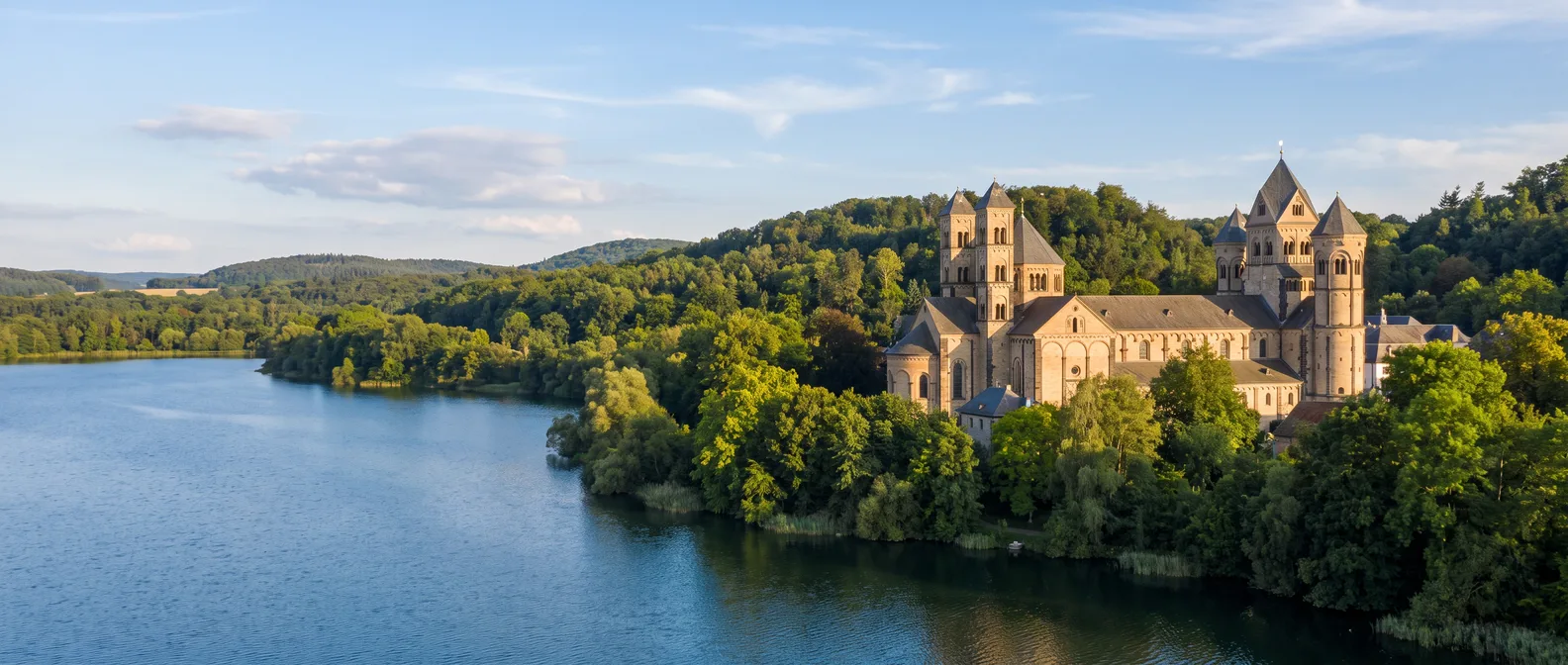 Romanische Abtei Maria Laach mit mehreren Türmen am bewaldeten Ufer des Laacher Sees