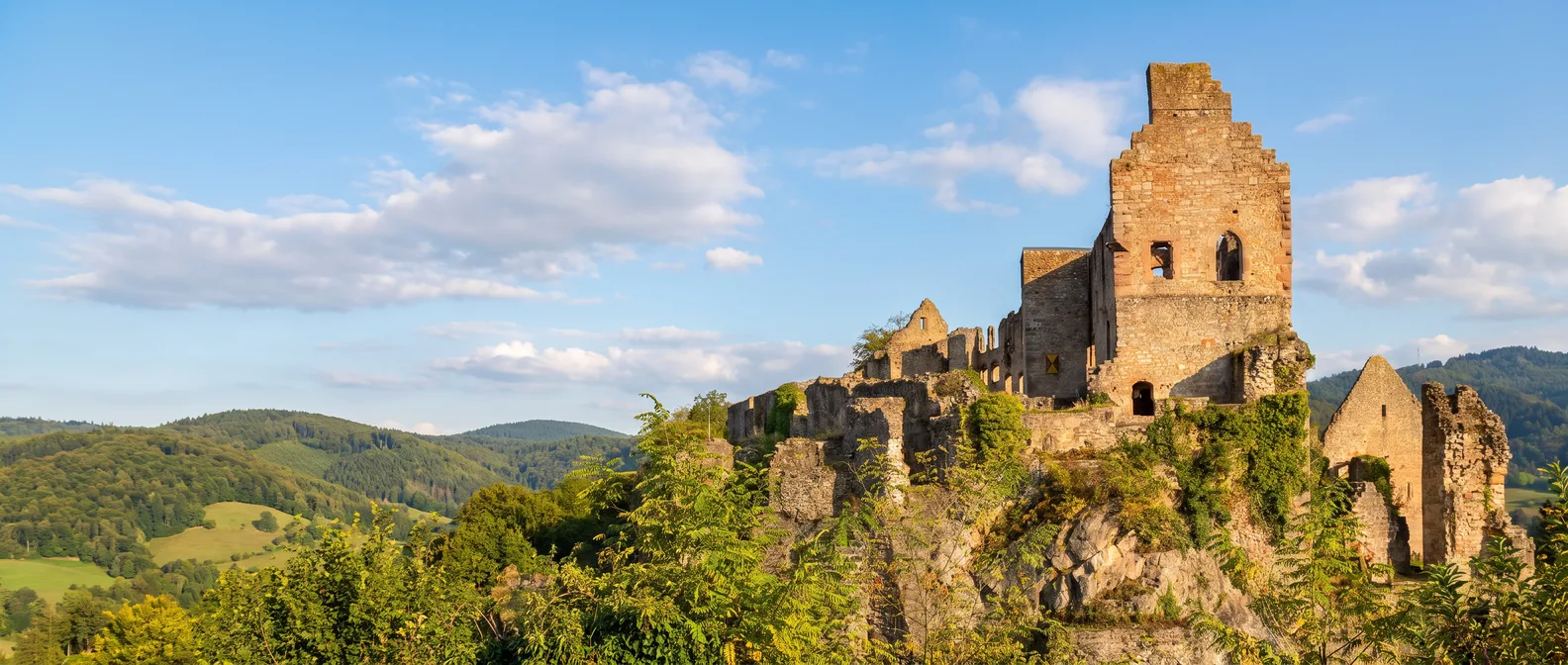 Die Burgruine Hochburg bei Emmendingen mit Bergfried und Stufengiebel auf einem bewachsenen Felsen vor den Hügeln des Schwarzwalds