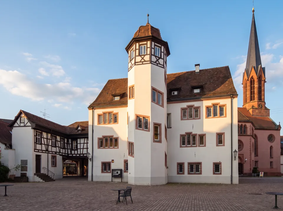 Das weiße Markgrafenschloss in Emmendingen mit achteckigem Treppenturm, daneben Fachwerkhäuser und der Turm der Stadtkirche