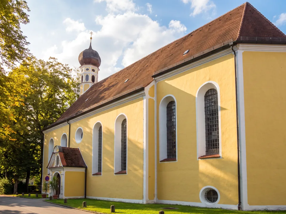 Die gelbe Wallfahrtskirche Heilig Blut in Erding mit weißem Zwiebelturm zwischen grünen Bäumen