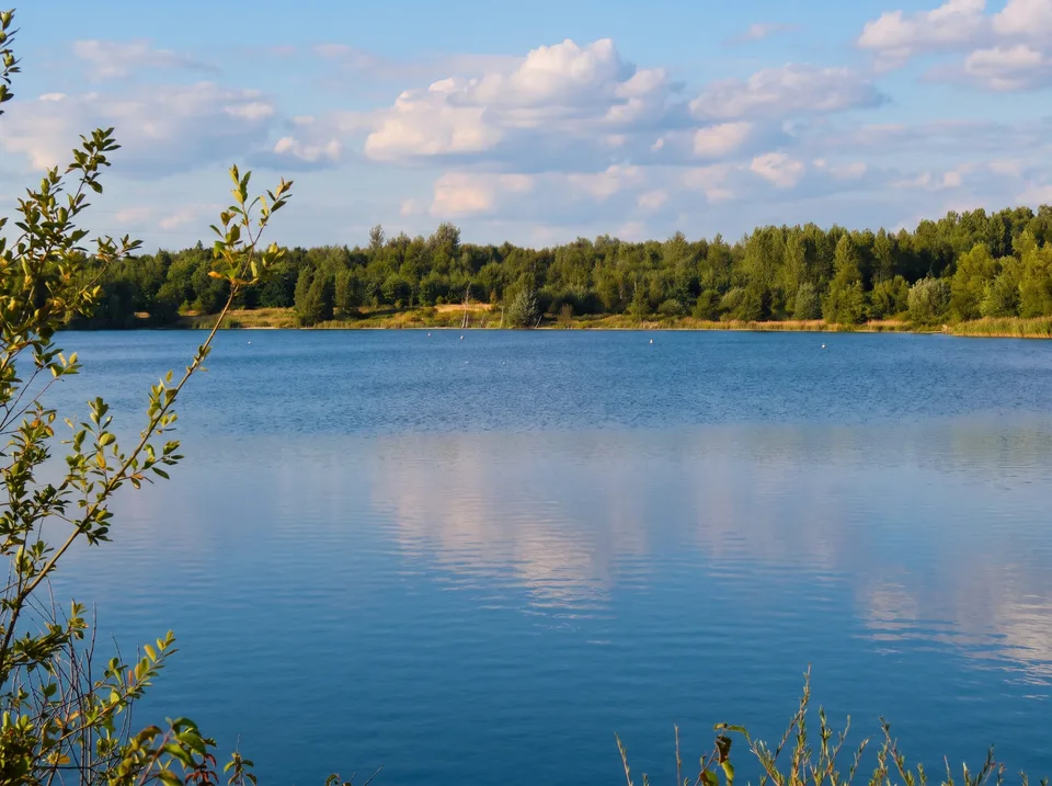 Blausteinsee bei Eschweiler mit ruhigem blauem Wasser und bewaldetem Ufer unter Sommerwolken