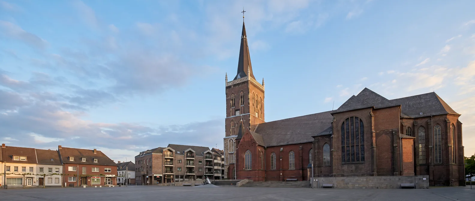 Backsteinkirche St. Peter und Paul in Eschweiler mit hohem Turm und spitzem Schieferhelm am Marktplatz unter blauem Himmel