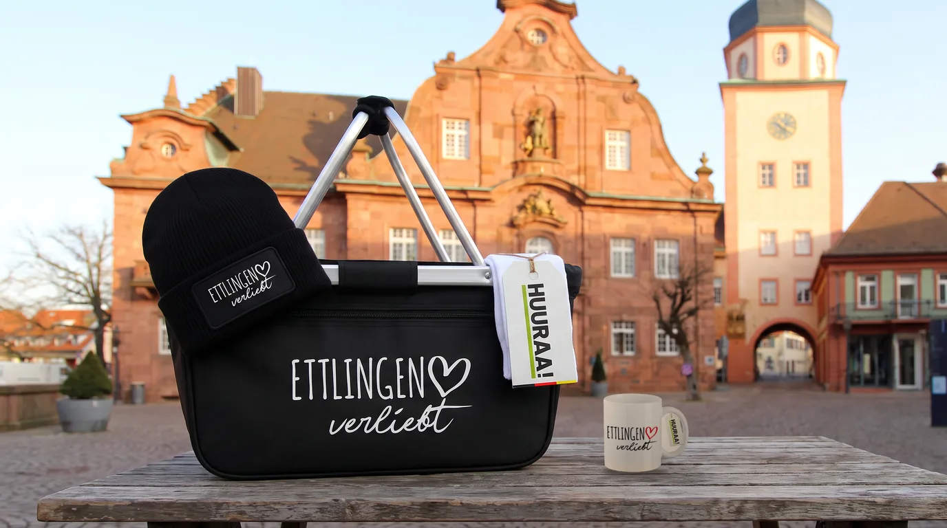 Schwarzer Einkaufskorb Ettlingen verliebt mit Beanie und Socken, daneben die weiße Kaffeetasse, auf einem Holztisch vor dem Ettlinger Rathaus