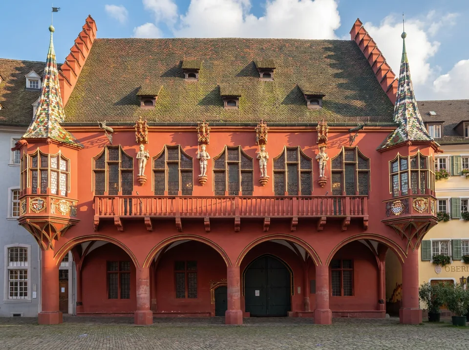 Das rote Historische Kaufhaus am Münsterplatz mit Arkaden, Statuen und bunt gedeckten Erkertürmchen