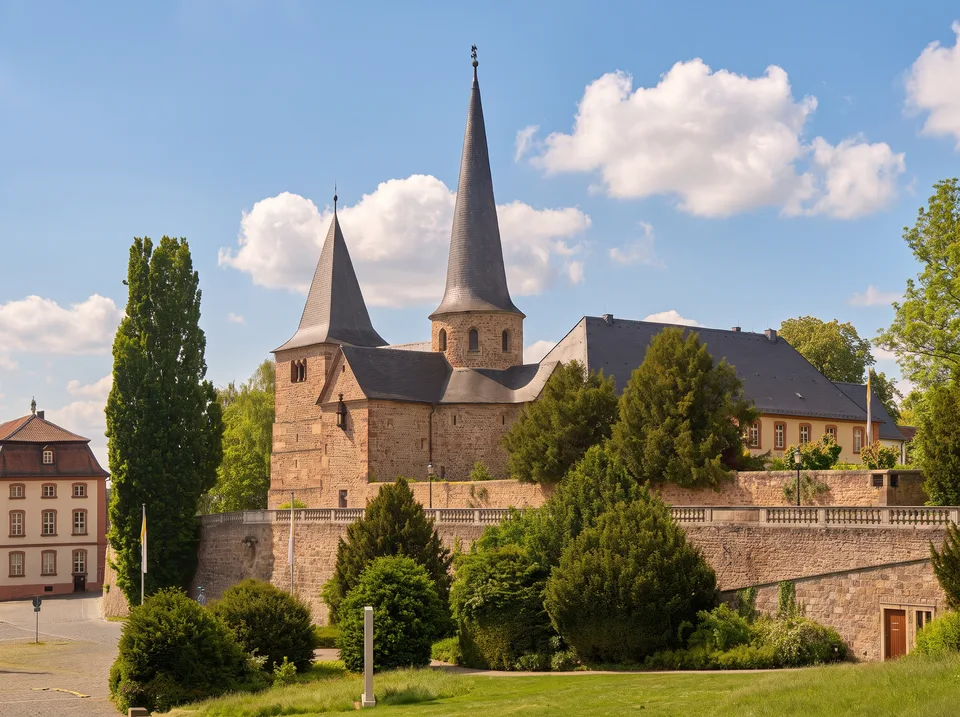 Die Michaelskirche in Fulda aus rötlichem Bruchstein mit zwei spitzen Türmen über der Terrassenmauer