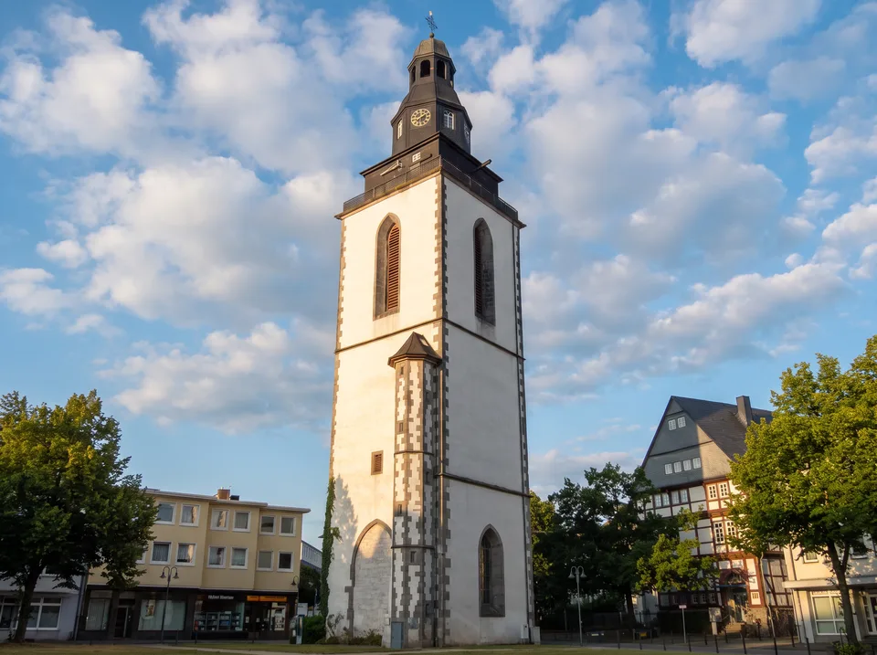 Weißer Stadtkirchenturm in Gießen mit dunkler Turmhaube und Uhr vor blauem Himmel