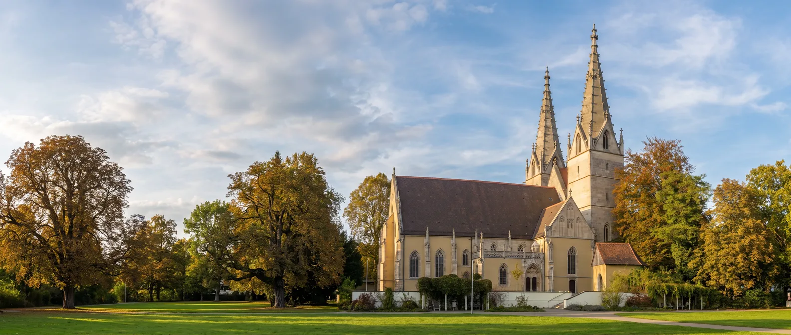 Oberhofenkirche in Göppingen mit zwei schlanken gotischen Steintürmen in einem Park mit alten Bäumen