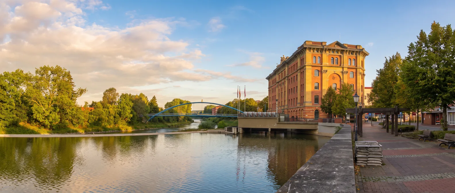 Die Pfortmühle aus rotem Backstein am Ufer der Weser in Hameln, links der ruhige Fluss mit Bogenbrücke unter blauem Himmel