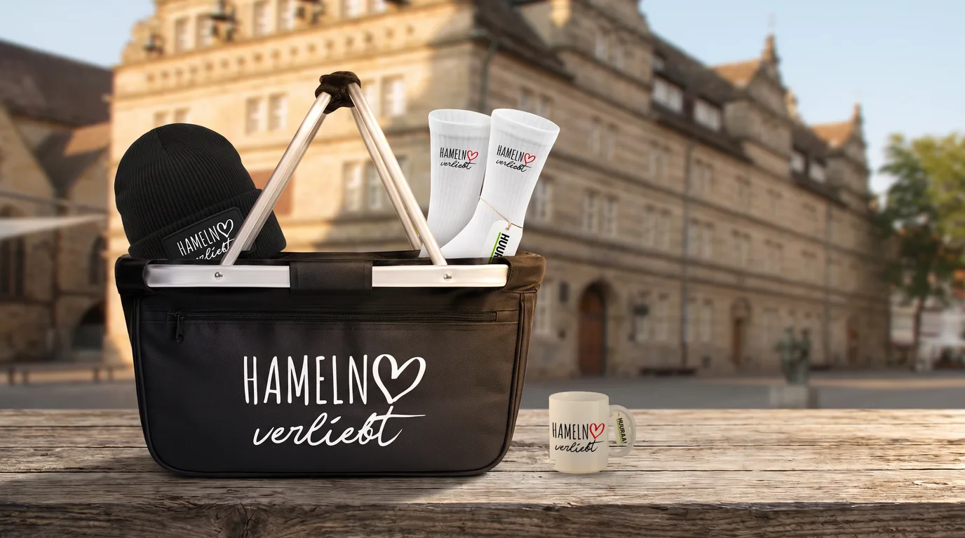 Schwarzer faltbarer Einkaufskorb „Hameln verliebt“ mit Beanie und Socken, daneben die Kaffeetasse, vor dem Hochzeitshaus in Hameln