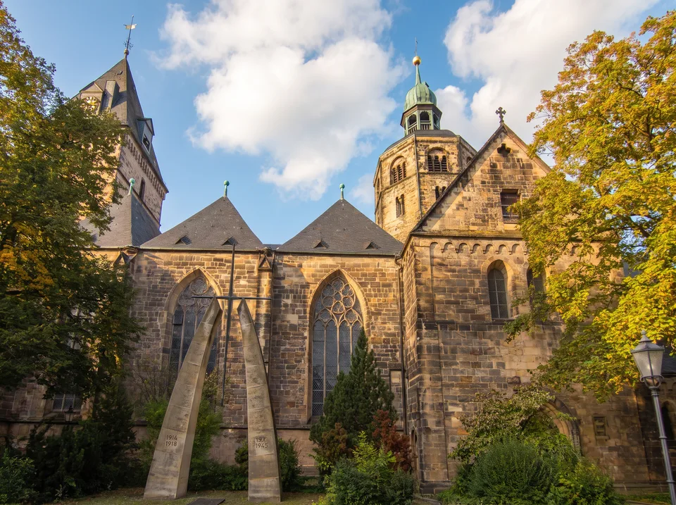 Gotisches Münster St. Bonifatius in Hameln aus Sandstein mit achteckigem Vierungsturm und spitzem Westturm zwischen Bäumen