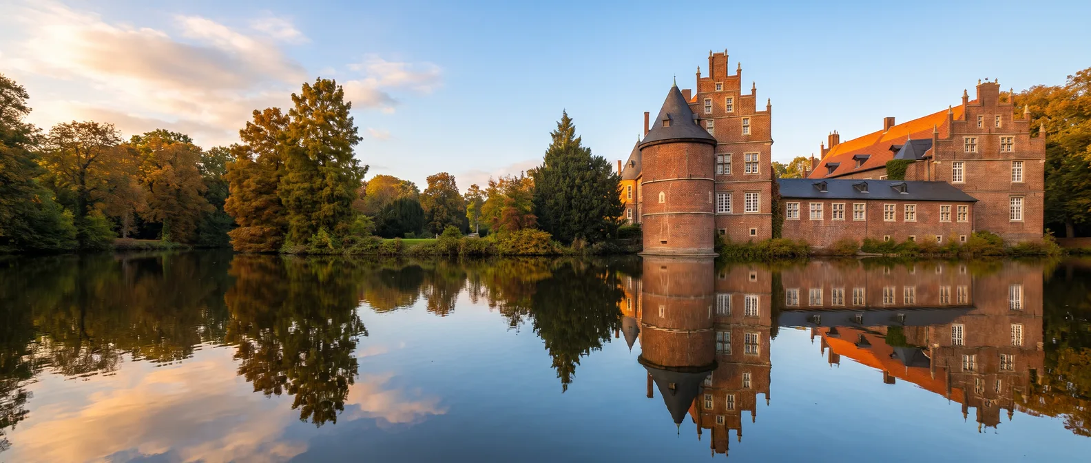 Wasserschloss Herten aus rotem Backstein mit rundem Turm und Treppengiebel, das sich im Schlossteich spiegelt