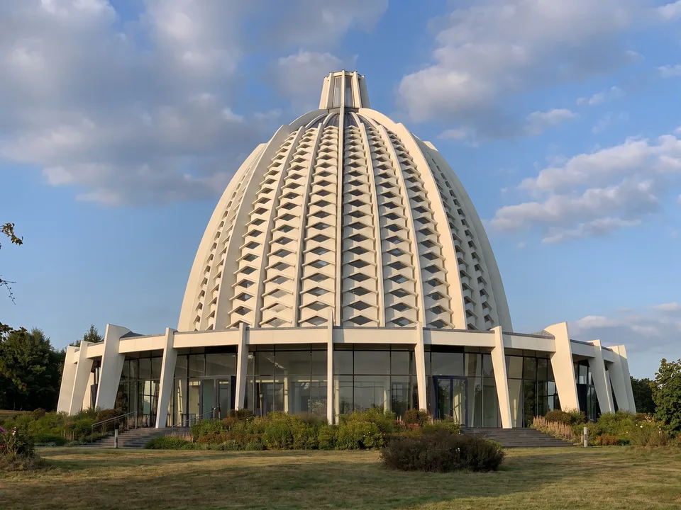 Das Haus der Andacht der Bahai in Hofheim-Langenhain mit weißer, gerippter Kuppel und gläsernem Erdgeschoss vor blauem Himmel