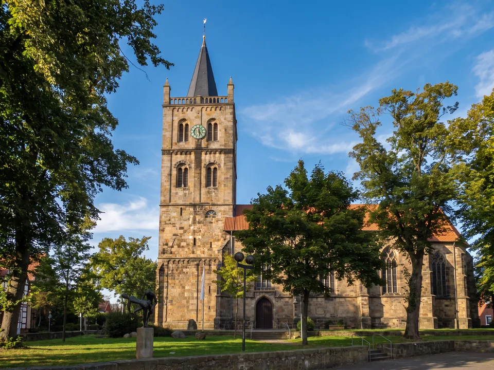 Evangelische Christuskirche in Ibbenbüren aus Sandstein mit hohem Westturm, Turmuhr und spitzem Schieferhelm hinter grünen Bäumen