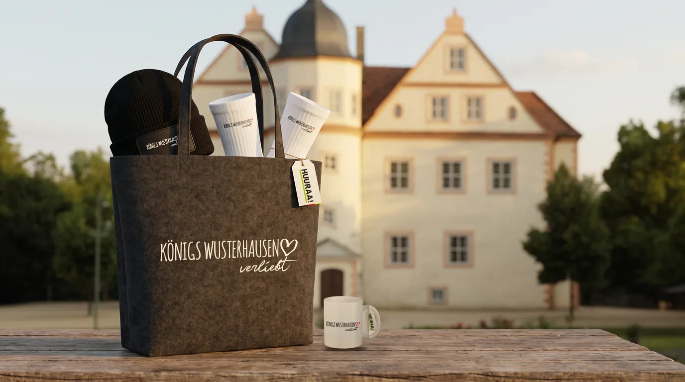 Grauer Filzshopper Königs Wusterhausen verliebt mit Beanie und Socken, daneben die weiße Kaffeetasse, auf einem Holztisch vor dem Schloss Königs Wusterhausen