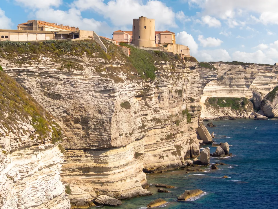 Die Oberstadt von Bonifacio mit rundem Turm auf den weißen, geschichteten Kalkfelsen über dem tiefblauen Meer