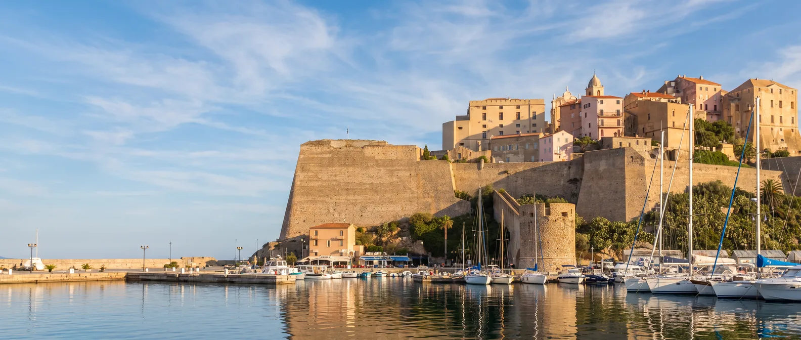 Die genuesische Zitadelle von Calvi mit mächtigen Mauern und Häusern der Oberstadt über dem Yachthafen im goldenen Abendlicht