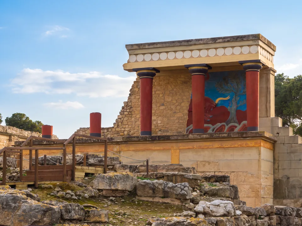 Rekonstruierter Nordeingang des Palastes von Knossos mit roten minoischen Säulen und Stierfresko unter blauem Himmel