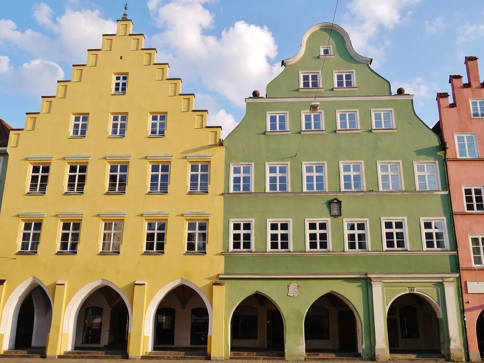 Farbige Giebelhäuser in der Landshuter Altstadt: gelbes Haus mit Treppengiebel und grünes Haus mit geschwungenem Giebel über Laubenbögen