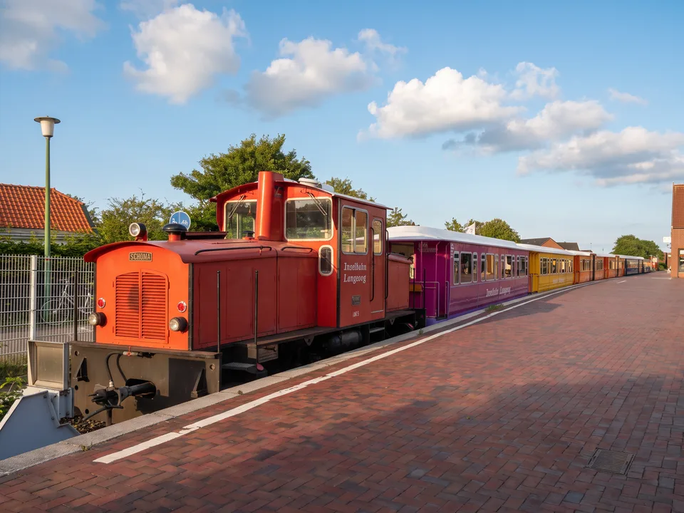 Rote Diesellok der Inselbahn Langeoog mit bunten Waggons am Bahnsteig des Inselbahnhofs