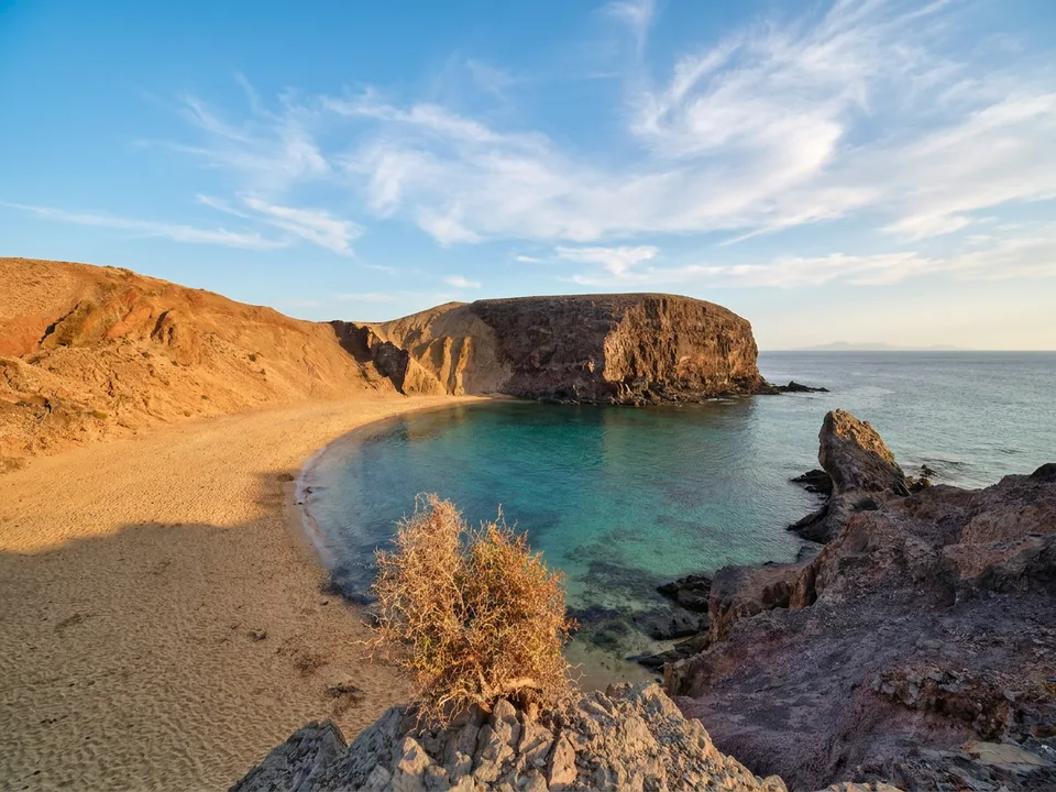 Goldene Sandbucht mit türkisfarbenem Wasser und braunen Vulkanklippen an den Papagayo-Stränden bei Playa Blanca