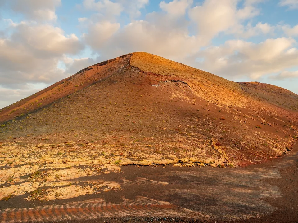 Rostroter Vulkankegel im Nationalpark Timanfaya auf Lanzarote unter blauem Himmel mit Wolken
