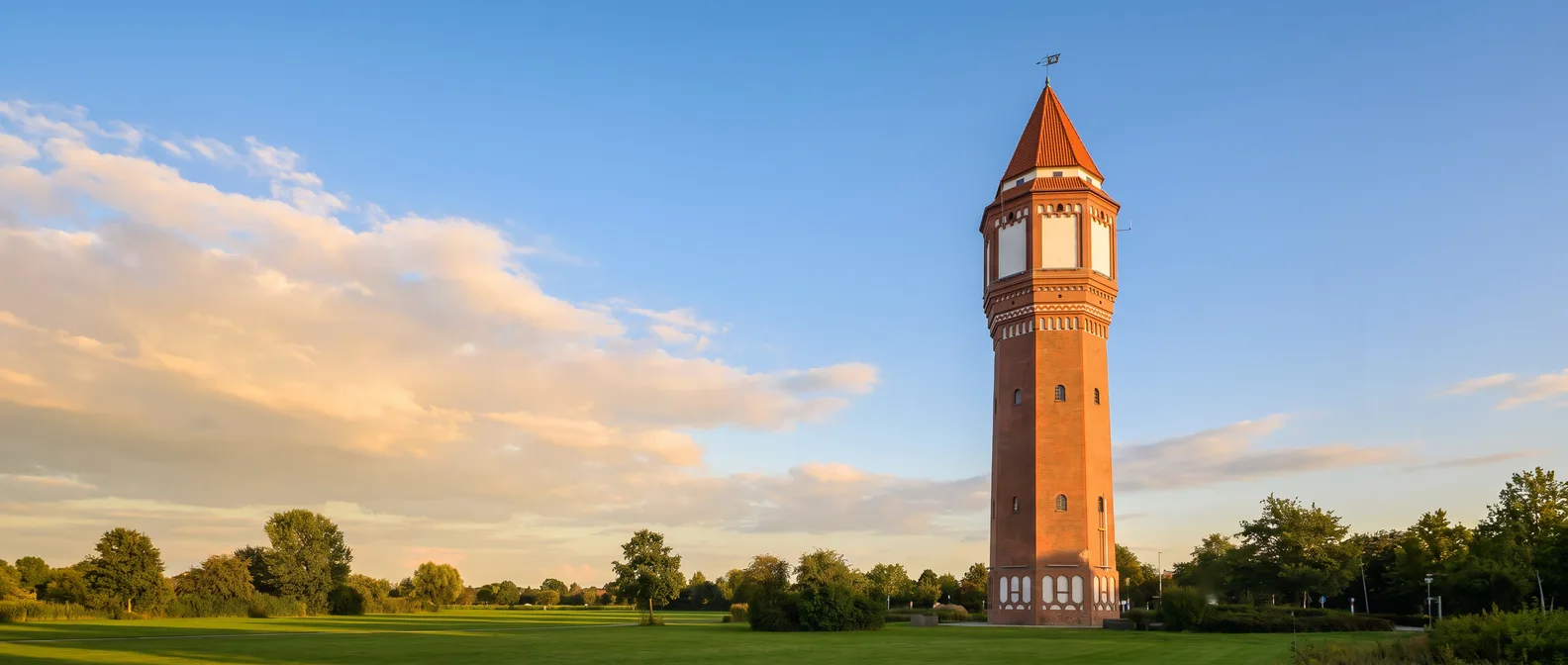 Lehrter Wasserturm, achteckiger Backsteinturm mit hellem Obergeschoss und spitzem roten Zeltdach, auf einer grünen Wiese im goldenen Abendlicht