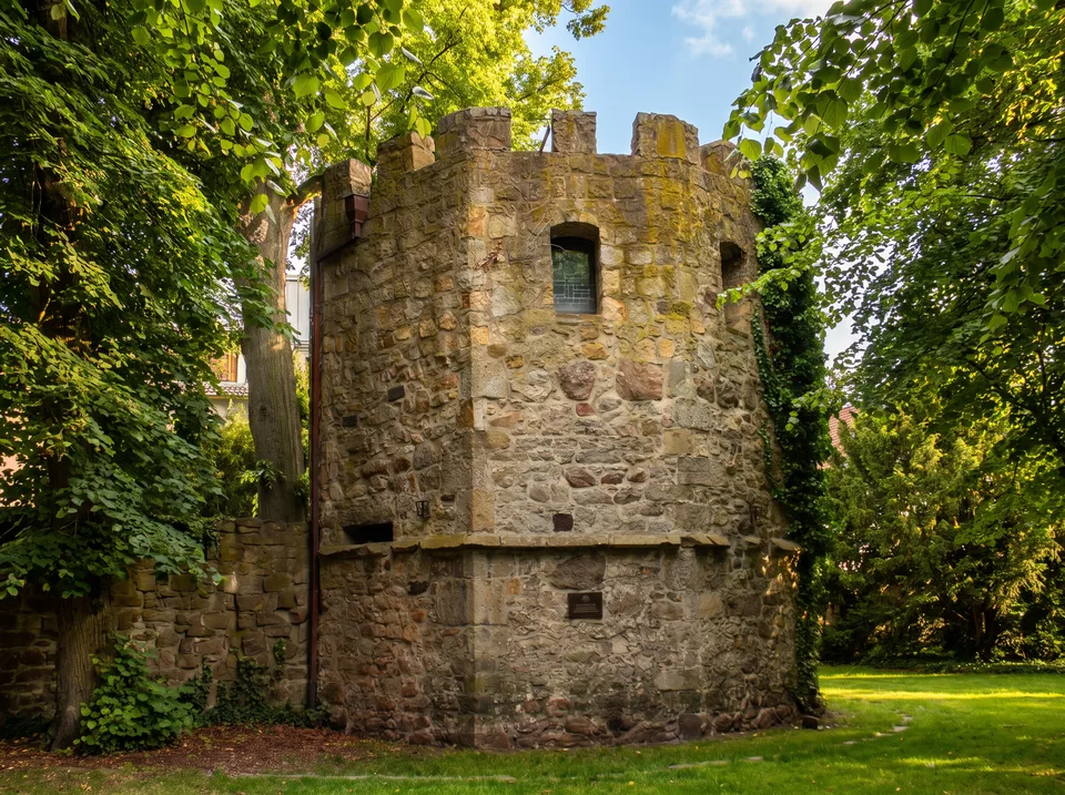 Der runde Pulverturm aus grob behauenem Sandstein mit Zinnenkranz zwischen alten Bäumen in Lingen